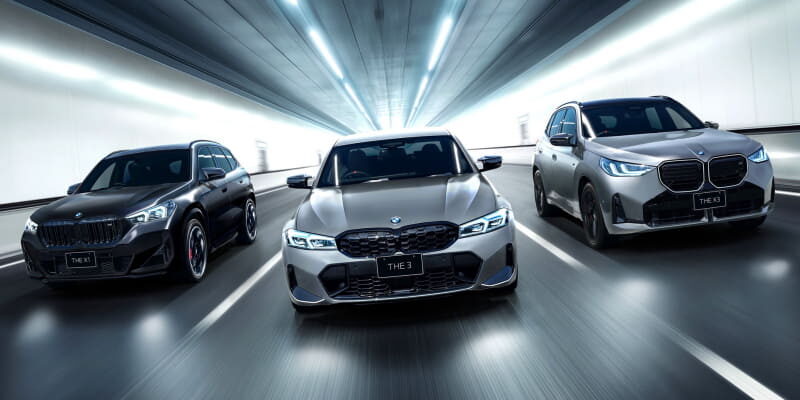 Three BMW cars driving side by side through a bright tunnel, motion blur trailing behind them, front-and-center bronze-colored model leading the pack.