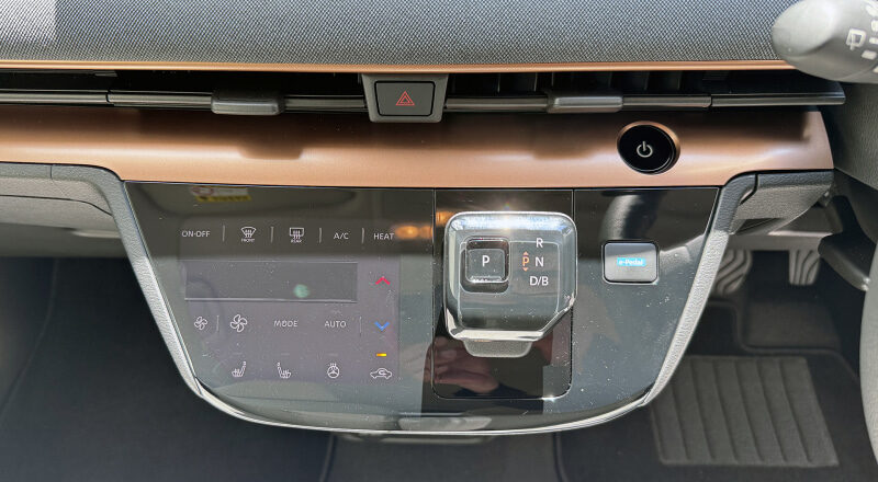 Center console of a car showing a digital climate control panel and a compact gear selector.