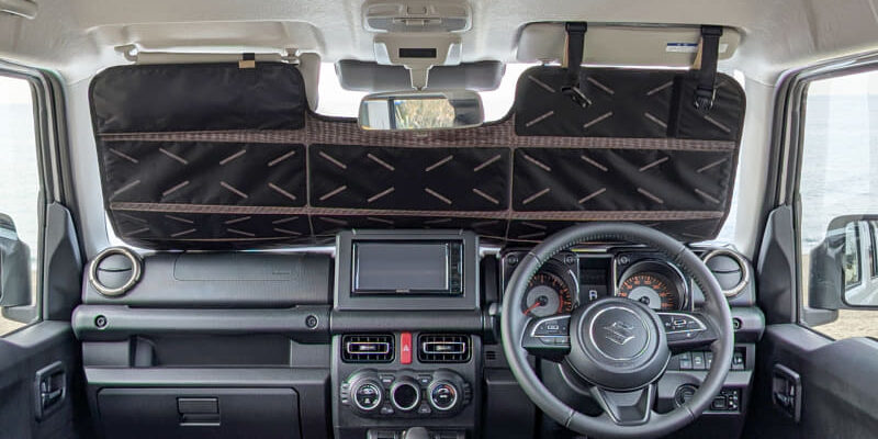 Interior of a right-hand-drive car with a large quilted black windshield organizer spanning the dashboard and sun visors.