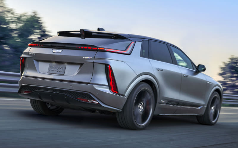 Silver SUV in motion, rear three-quarter view on a highway with a prominent spoiler and red taillights.