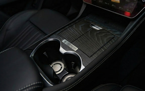 Close-up of a car center console with two cup holders, a small storage area, and leather trim.