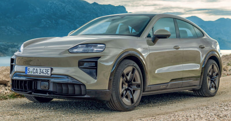 Front three-quarter view of a gray electric SUV parked on a gravel road with mountains in the background.