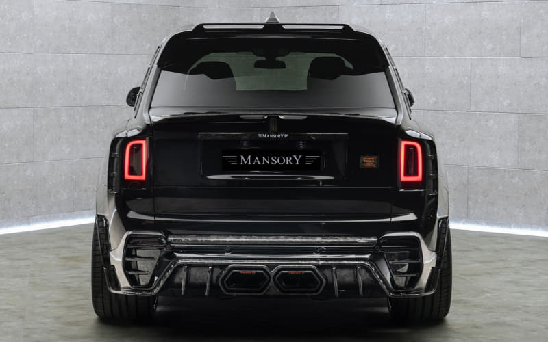 Black SUV viewed from the rear with vertical red taillights and a Mansory badge on the tailgate in a showroom setting.