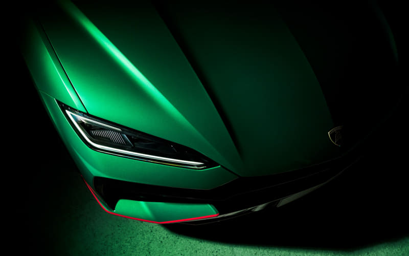 Close-up of a neon-green sports car front end, showing an angular hood and sleek headlight under dramatic lighting.