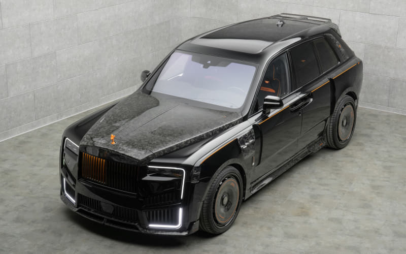 Black luxury SUV with orange trim accents and dusty hood parked in a gray, concrete-walled studio