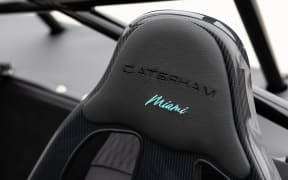 Close-up of a black sports car seat headrest with 'CAYMAN' embroidery and turquoise 'Miami' text.