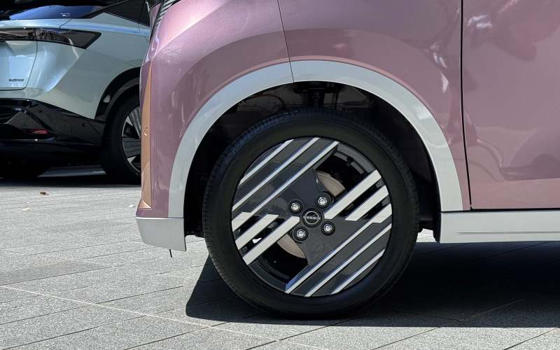 Close-up of a pink car's front wheel with a distinctive diagonal-striped alloy rim on a paved surface.