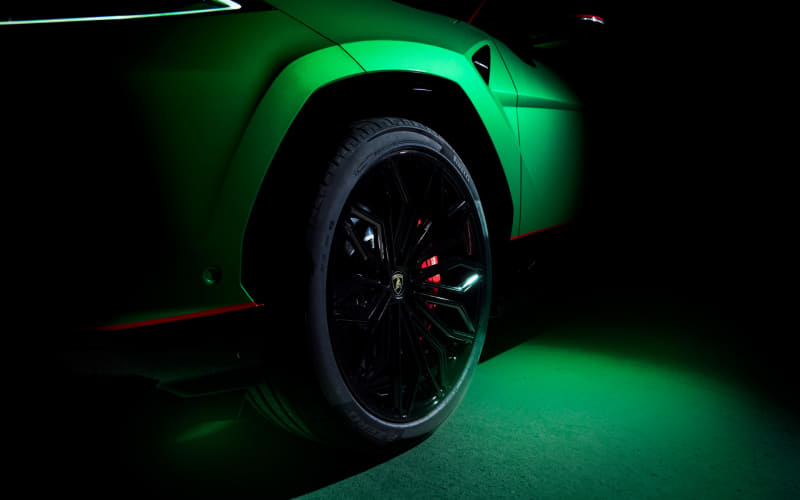 Close-up of a bright green sports car wheel with a black rim and red brake calipers under neon green lighting in a dark setting.