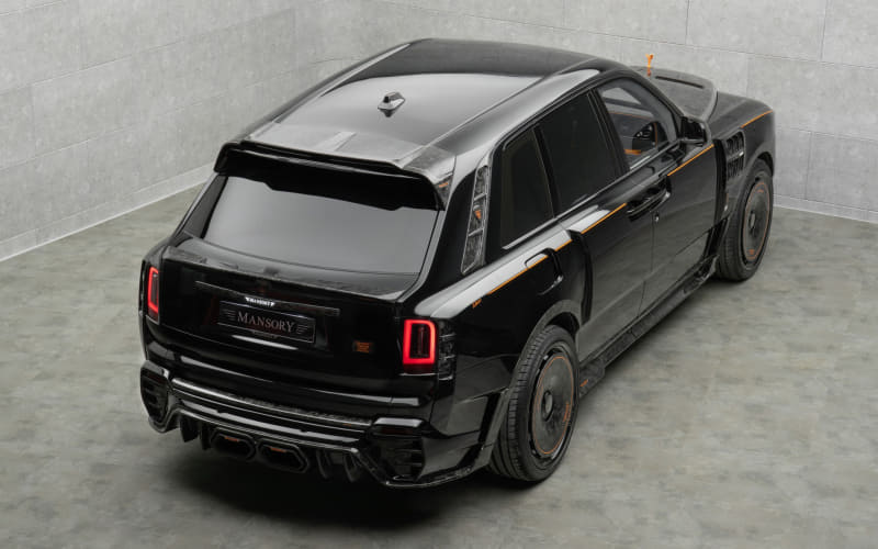Black Mansory-modified luxury SUV, rear-three-quarter view in a showroom, with a wide body kit and orange accents.