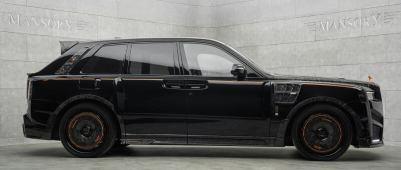 Black luxury SUV customized by Mansory, with orange accents and tinted windows in a showroom setting.