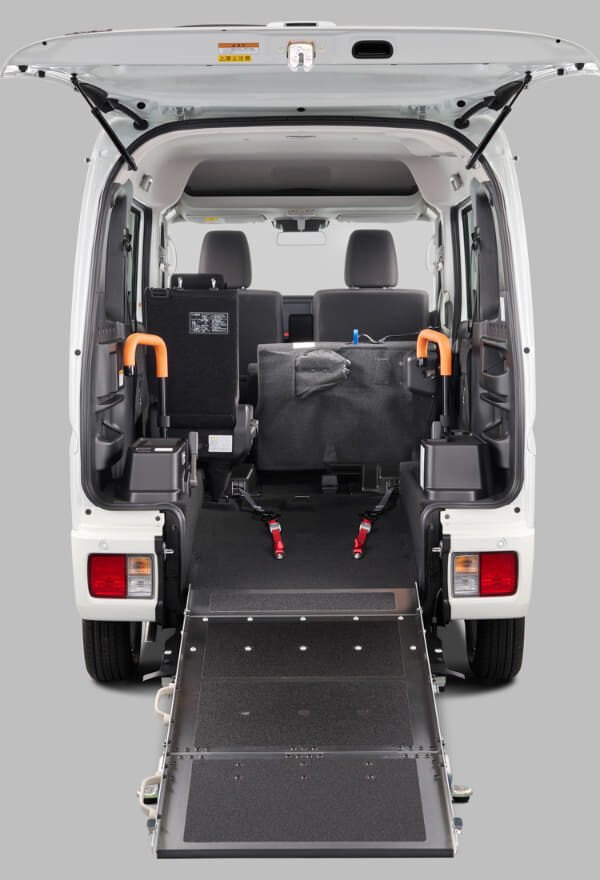 Rear view of a white wheelchair-accessible van with the ramp extended to the ground and orange handrails visible inside the doorway.