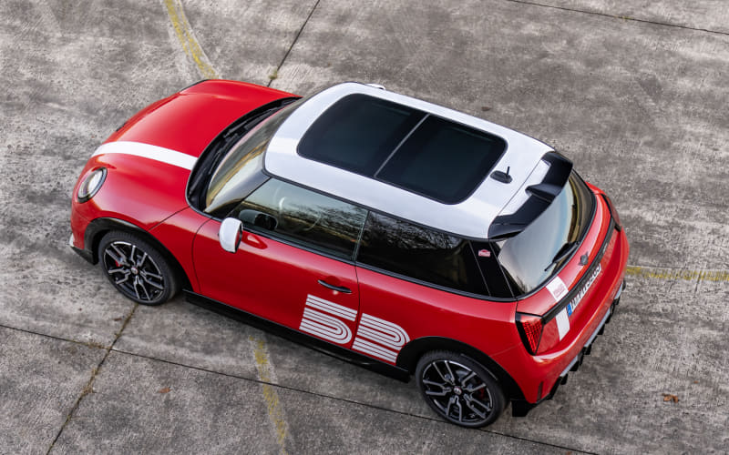 Overhead view of a red Mini Cooper-style car with a white roof and bold white racing graphics on the side.