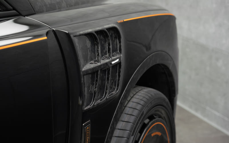 Close-up of a black vehicle's front fender with orange trim and side vent, showing the wheel and tire.