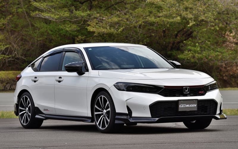 Three-quarter front view of a white Honda sedan with Mugen styling, parked on a paved lot with trees in the background.