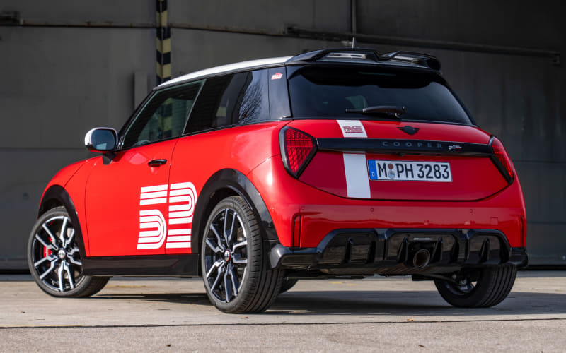 Rear three-quarter view of a red compact SUV with a white racing stripe and side graphic, parked on concrete near an industrial backdrop.