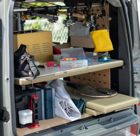 Interior of a van turned into a mobile workshop: shelves, a pegboard, and various tools and supplies tucked into the back.