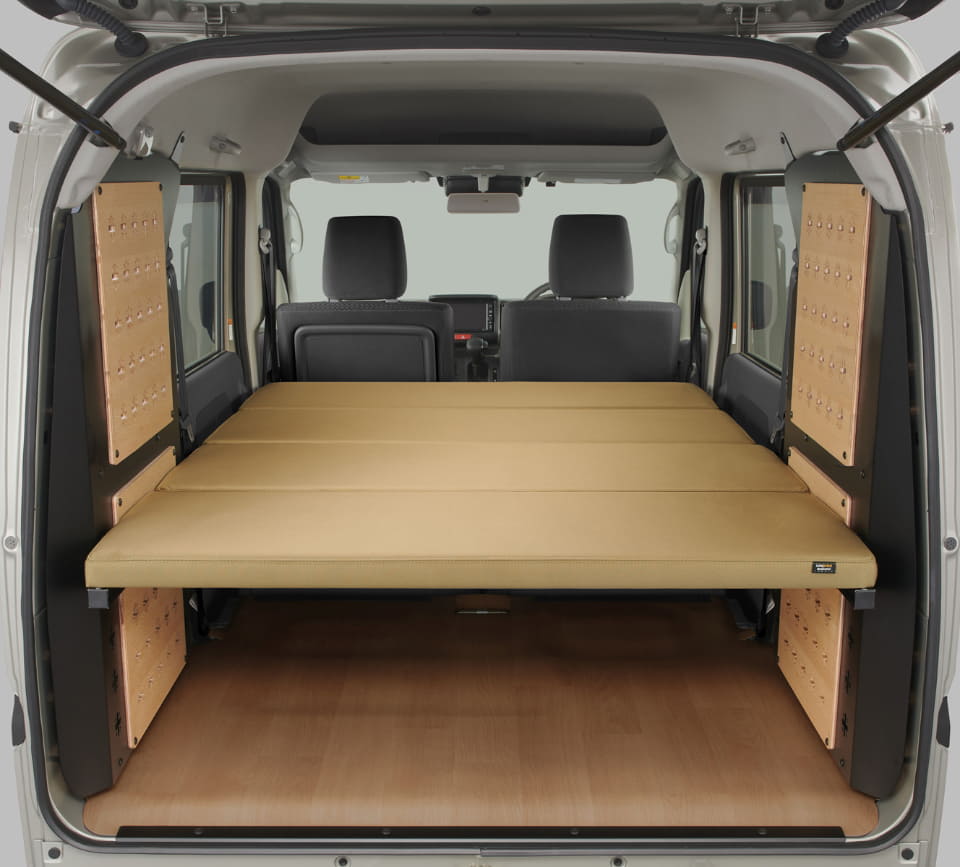 Camper van interior with a flat beige bed platform across the rear cargo area and wooden side panels for sleeping.
