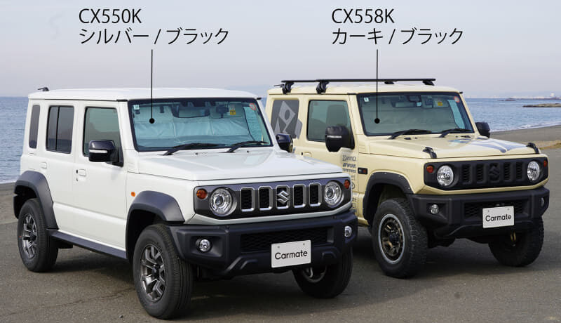 Two Suzuki off-road SUVs parked on a sandy beach: white CX550K (silver/black) and beige CX558K (khaki/black), with model labels above them.