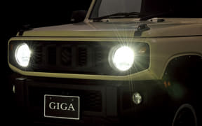 Front view of a dark car with two bright headlights on at night and a 'GIGA' license plate.
