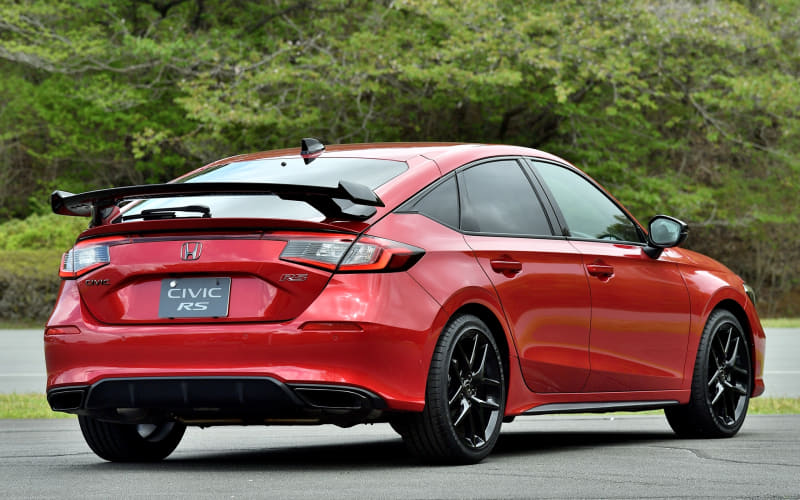 Red Honda Civic RS rear view with a large spoiler, parked on a paved surface with green trees in the background.