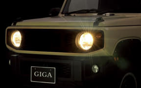 Front view of a white car with headlights on, nighttime scene, license plate reads GIGA.