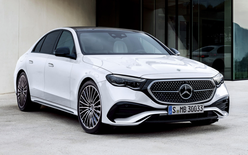 White Mercedes-Benz sedan with a chrome grille parked in front of a modern glass building outside a dealership. (Front 3/4 view)