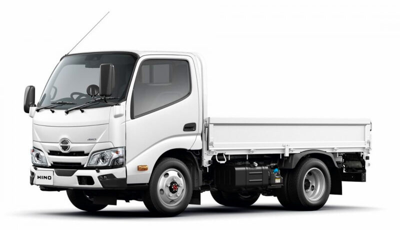 Front-left view of a white Hino flatbed truck isolated on a white background, cab and cargo bed visible.