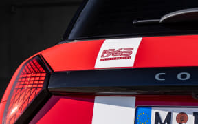 Rear of a red car with a white stripe, RS badge on the trunk and a partial European license plate visible.