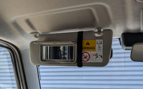 Front sun visor with mirror open, showing an airbag warning sticker.