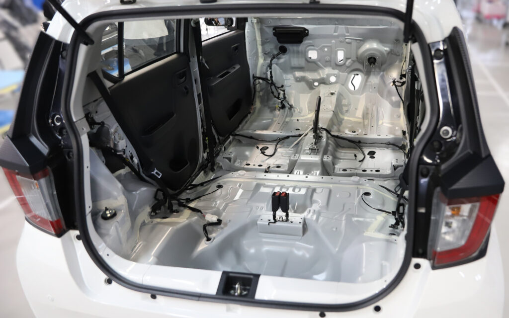Rear interior of a white SUV with back seats removed, exposing the bare metal frame, wiring, and mounting points in the trunk area.