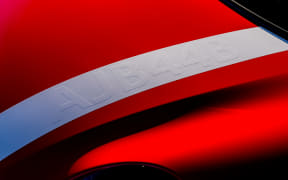 Close-up of a red car body with a white curved racing stripe and dark shadows, highlighting sleek design.