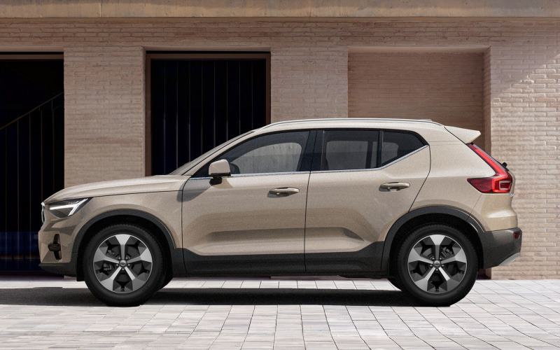 Side profile of a beige compact SUV parked on a paved driveway in front of a brick building.