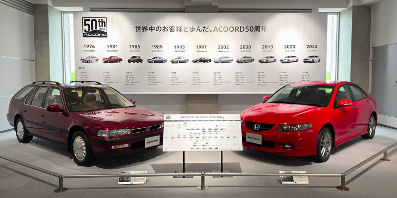 Two Honda Accord cars (maroon wagon and red sedan) are on display in a showroom beside a timeline banner celebrating 50 years of the Accord.