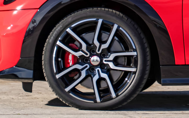 Close-up of a red car wheel with a black and silver multi-spoke alloy rim and a red brake caliper behind the spokes, MINI center cap visible.