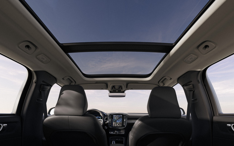 View from back seats looking toward the dashboard of a car with a panoramic sunroof; blue sky seen through the glass roof.