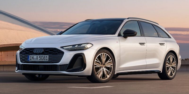 White Audi estate car (Avant) parked on a rooftop with a sunset sky in the background, front three-quarter view.",