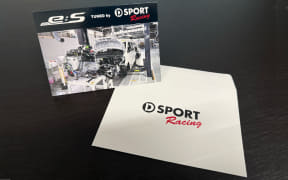 Boxed racing toy product with a photo of a car on the box, placed next to a white envelope bearing the SPORT Racing logo.