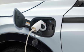 Blue electric car being charged with a white charging plug connected to the front port on the driver's side.