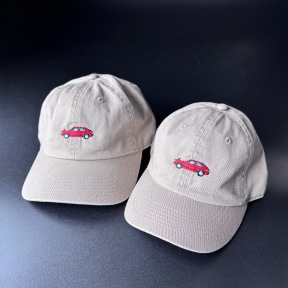 Two beige baseball caps with a small red car embroidery on the front, placed on a dark blue surface.