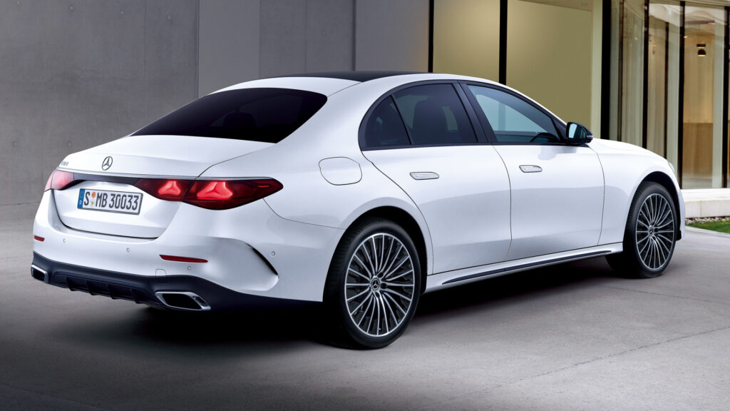 Rear three-quarter view of a white luxury sedan with dark tinted windows parked outdoors near a modern building.