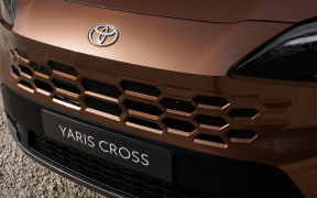 Front view of a brown Toyota Yaris Cross, showcasing the hexagonal grille, Toyota emblem, and the 'YARIS CROSS' text on the plate area