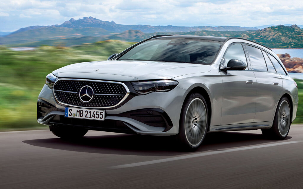 Silver Mercedes-Benz station wagon driving on a highway with a blurred green landscape and mountains in the distance.