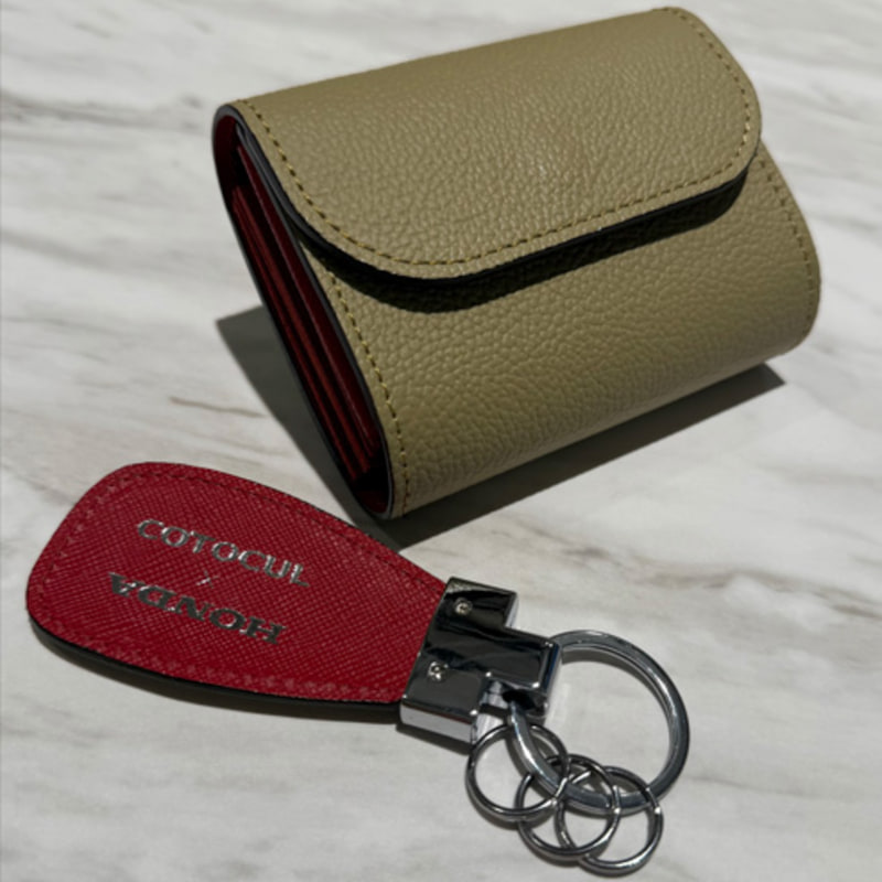 Beige textured leather wallet with a red key fob and metal key ring on a light marble surface.