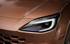 Close-up of a bronze-brown car's headlight and front grille, showing the sleek design and metallic paint.
