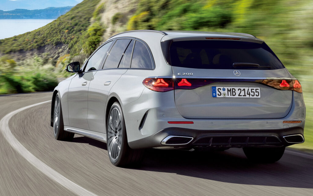Rear three-quarter view of a silver Mercedes-Benz E200 wagon driving on a curving mountain road.