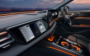 Modern car interior at dusk with ambient orange lighting, a large central touchscreen, and a digital instrument cluster.