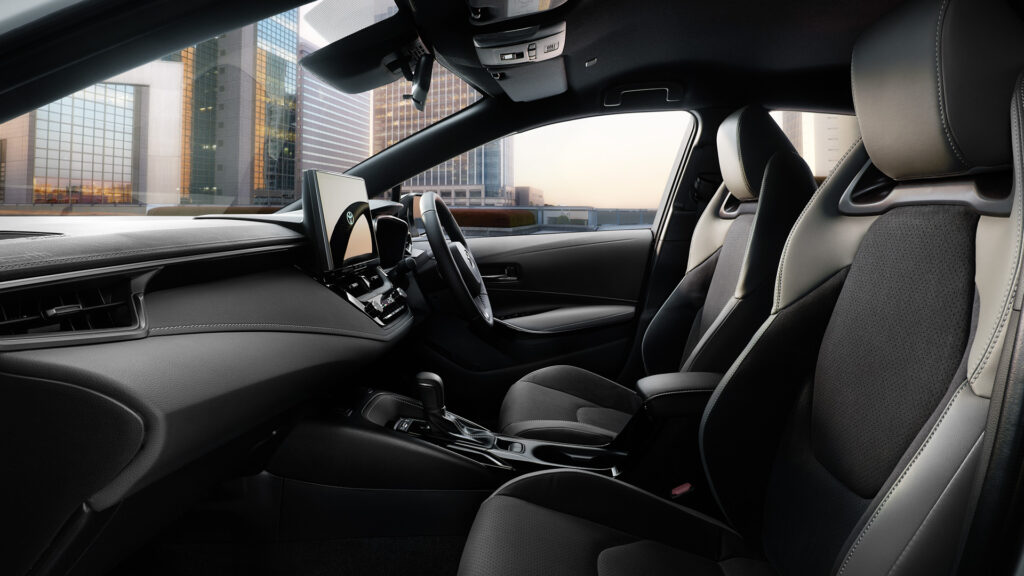 Interior of a modern car with black leather seats, stitched dashboard, and a city skyline visible through the windshield.
