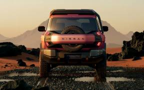 Front view of a red Nissan off-road pickup driving toward the camera on a rocky desert at sunset.