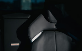 Close-up of a car seat in a dark interior, showing the headrest and backrest with soft light reflecting on the leather.