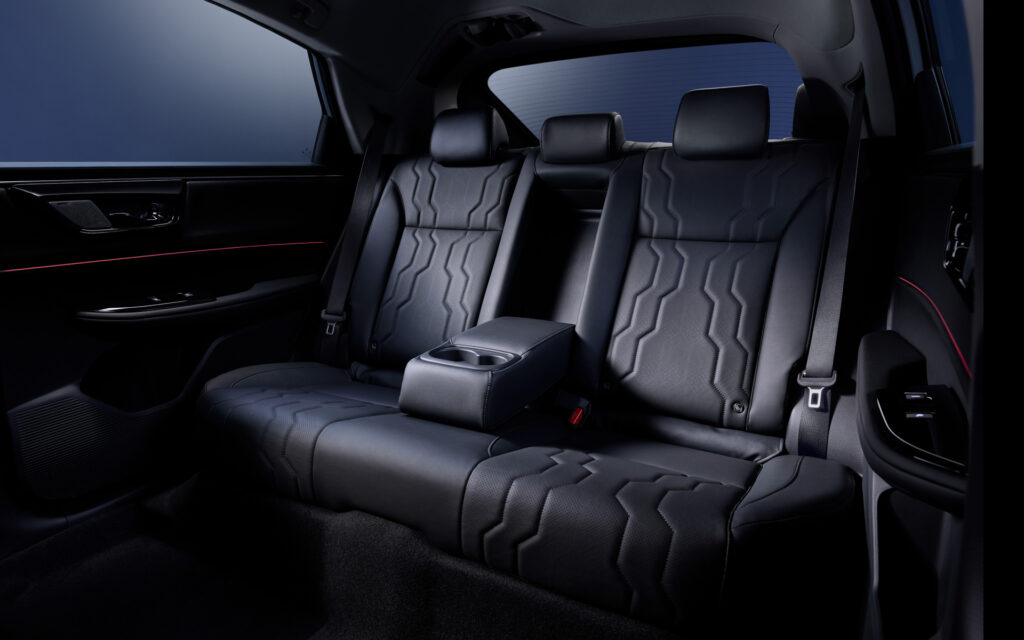 Dark leather car rear seats with a fold-down center armrest and built-in cupholders; three headrests and visible seat belts in a luxury sedan interior.